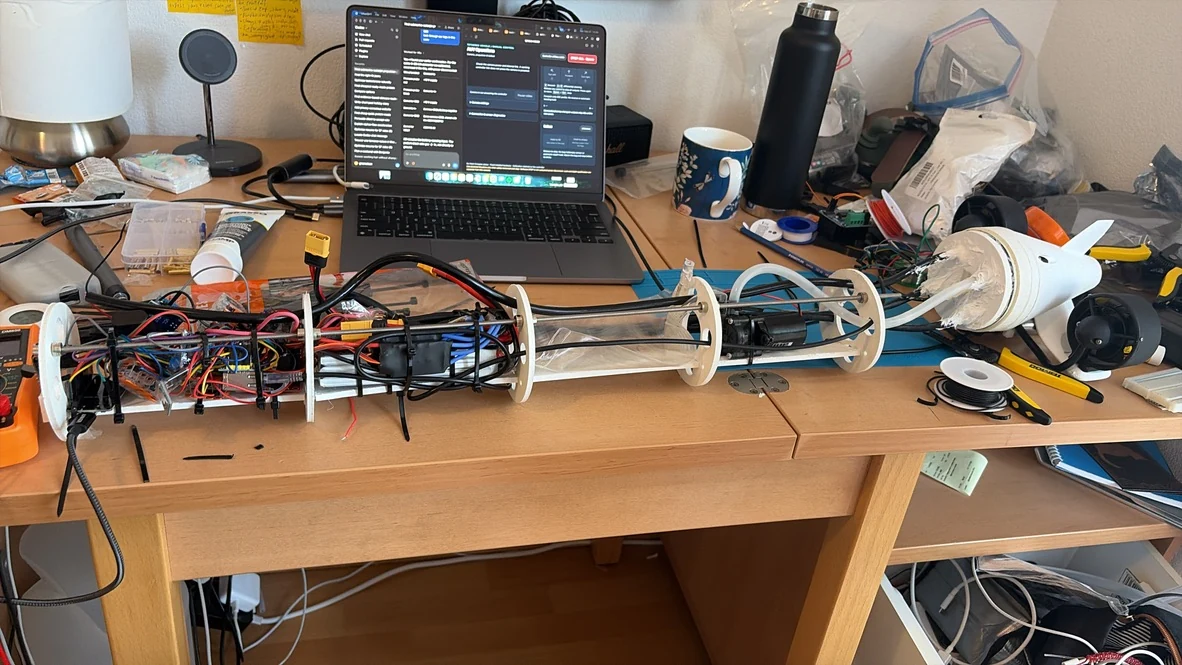 AUV internals with the electronics sled, battery, ballast bag, pump, and twin-thruster tail laid out on the workbench