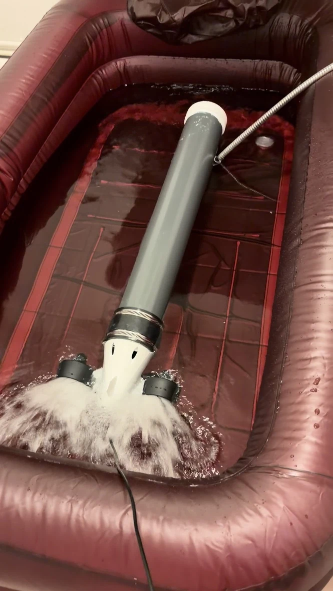 The assembled grey PVC underwater vehicle in a shallow inflatable pool, with water flowing behind its two rear thrusters